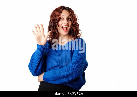 Happy woman wearing pullover sweater standing isolated over white background smiling broadly while waving raised palm, greeting friend. Saying hello, Stock Photo