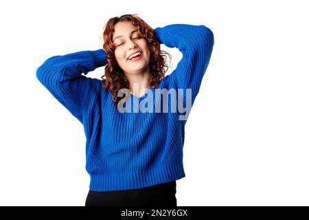 Happy woman wearing blue knitted sweater standing isolated over white background holding hands behind head and looking to the camera with big smiles. Stock Photo