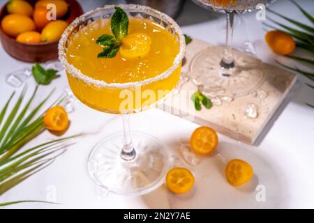 Sweet and salted Kumquat margarita cocktail garnished with kumquat slices  and mint, on marble and dark green tropical palm decorated background copy Stock Photo