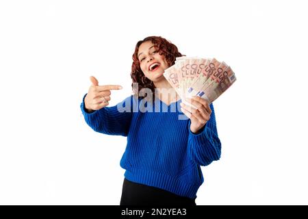 Young girl smiling happy wearing blue pullover sweater isolated over white background points to the banknotes or money with her index finger. She has Stock Photo