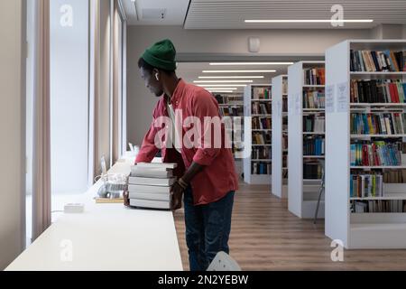 Young diligent African American man stands in library room preparing scientific report for college Stock Photo
