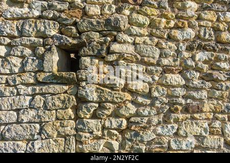Random stone wall of outhouse with small open window opening - France. Stock Photo