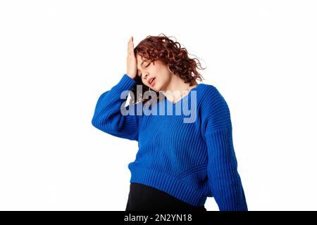 Portrait of woman wearing blue knitted sweater standing isolated over white background making facepalm gesture with hand. Face palm concept. Stock Photo