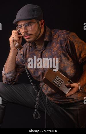 A man using a vintage landline telephone, holding the handset and base, looking concerned while making a call. Concept of old-fashioned communication, Stock Photo