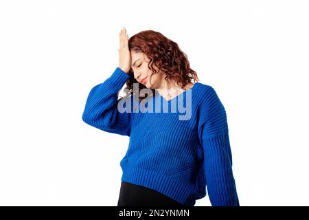 Portrait of young woman wearing blue knitted sweater standing isolated over white background making facepalm gesture with hand. Face palm concept. Stock Photo