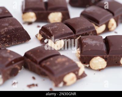 Broken pieces of  dark chocolate with hazelnuts on a white plate. Close up. Stock Photo