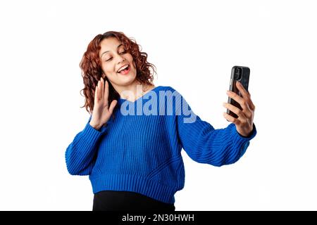 Young woman wearing blue pullover sweater isolated over white background using smartphone for video call. Video chatting, speaking on mobile phone via Stock Photo