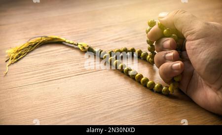 Selective focus of hand counting rosary beads on wooden background. Stock Photo