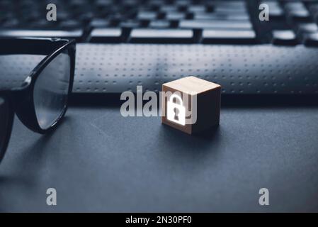 Computer security concept. A wooden cube with glowing padlock icon and glasses on a computer keyboard. Stock Photo