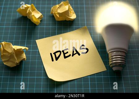 Ideas concept with a bright bulb and yellow memo note on a green craft mat. Stock Photo