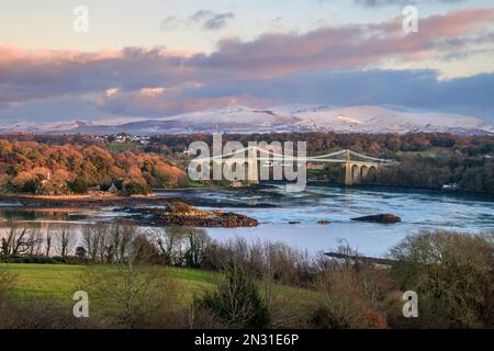 The Telford Bridge over the Menai Strait at sunset with the snow covered Snowdonia mountains in the background, Anglesey, North Wales Stock Photo