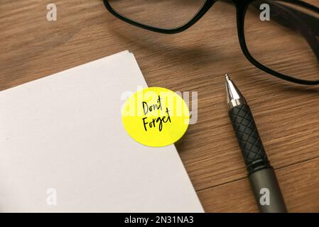 Green label sticker written with Don't Forget on a notebook with pen and glasses on wooden background. Stock Photo