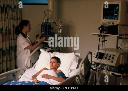 Medical nurse with young boy patient in hospital intensive care ward. Stock Photo