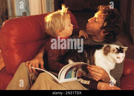 Man and boy indoors at home with pet cat. Stock Photo