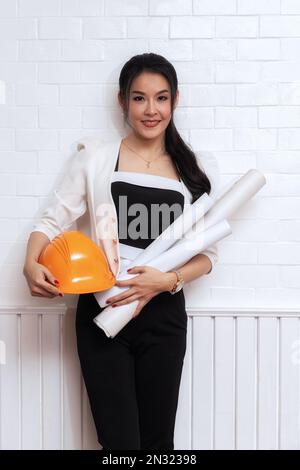 Female architect or engineer holding blueprints at the wall. Stock Photo