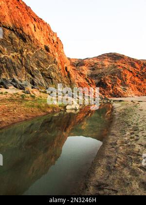 Reflections of the barren canyon cliffs in a pool in the Fish River of Namibia in winter in the early morning golden light Stock Photo