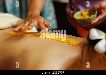 Close up of Spa therapist applying scrub salt on young woman back at salon spa. Hands massaging female back with scrub. Stock Photo
