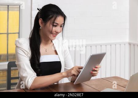 Beautiful young Asian working with tablet computer at office desk or co working space. Stock Photo