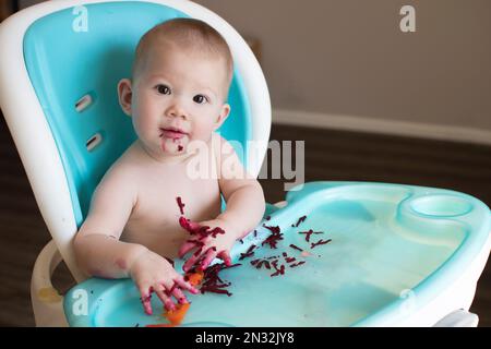 Baby eating solid foods in a high chair. Baby-led weaning. Baby eating healthy Stock Photo