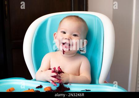 Baby eating solid foods in a high chair. Baby-led weaning. Baby eating healthy Stock Photo