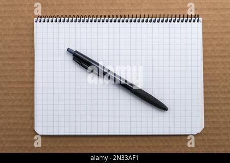 Graph paper spiral Notebook with black ballpoint pen on top of brown cardboard, top view. Stock Photo