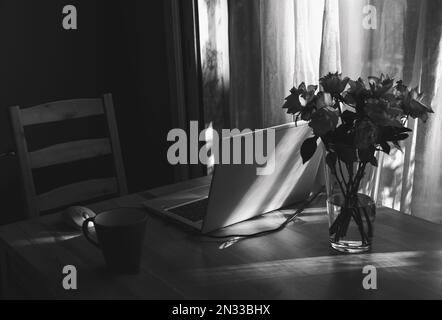 Simple candid workplace at home with laptop computer in sunset light. Remote working from home in comfortable working environment. Black white Stock Photo