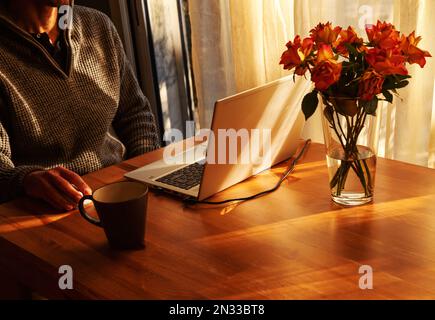 Man working from home at simple candid workplace with laptop computer in sunset light. Remote working from home in comfortable working environment Stock Photo