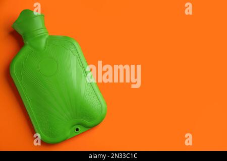 Green rubber hot water bottle on orange background, top view. Space for text Stock Photo