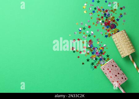 Colorful confetti and party crackers on green background, flat lay. Space for text Stock Photo