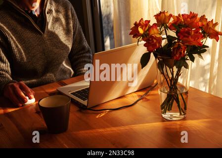 Man working from home at simple candid workplace with laptop computer in sunset light. Remote working from home in comfortable working environment Stock Photo