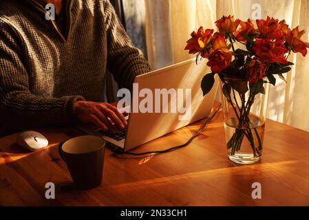 Man working from home at simple candid workplace with laptop computer in sunset light. Remote working from home in comfortable working environment Stock Photo