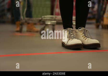 Woman standing behind taped floor marking in store for social distance, closeup. Preventive measure during coronavirus pandemic Stock Photo