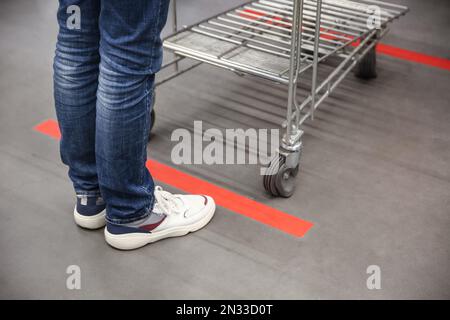 Person with shopping cart standing behind taped floor marking in store for social distance, closeup. Preventive measure during coronavirus pandemic Stock Photo