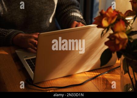 Man working from home at simple candid workplace with laptop computer in sunset light. Remote working from home in comfortable working environment. Stock Photo