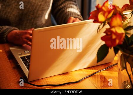 Man working from home at simple candid workplace with laptop computer in sunset light. Remote working from home in comfortable working environment. Stock Photo