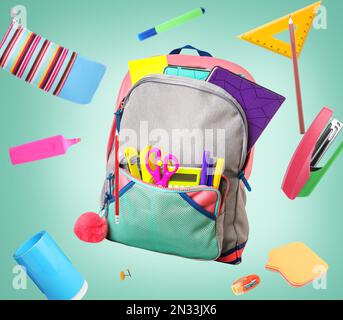 Backpack surrounded by flying school stationery on pale green background Stock Photo