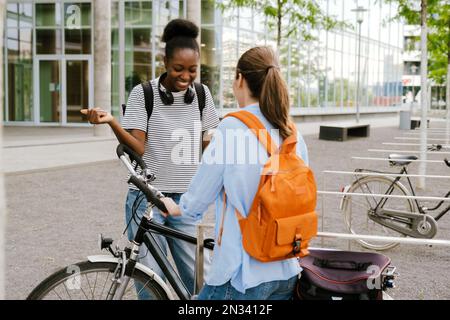 Young multiracial women with bicycle laughing while standing at city street Stock Photo
