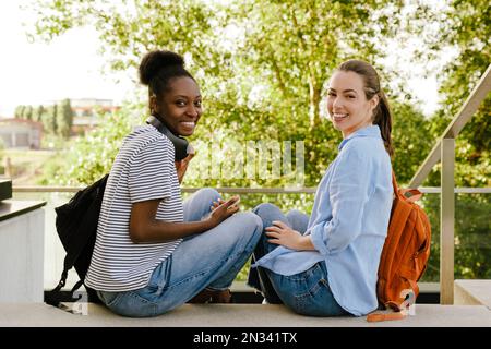 Young multiracial women smiling and using cellphone while sitting at park Stock Photo