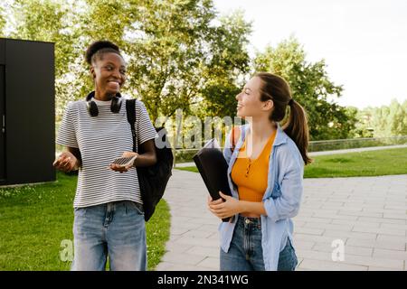 Young multiracial women smiling and talking while walking together at park Stock Photo
