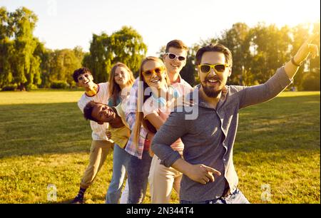 Funny and cheerful joyful company of young friends have fun together on green lawn in park. Stock Photo