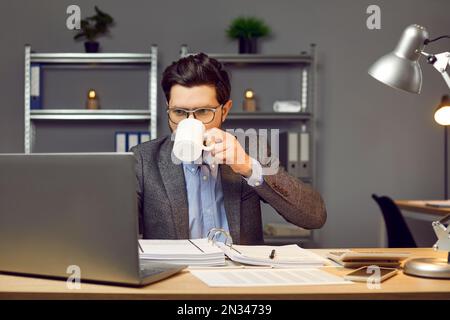 Busy young man working in the office, using a laptop computer, and drinking coffee Stock Photo