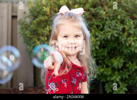 Little girl playing with bubbles. Happy child popping bubbles. Stock Photo