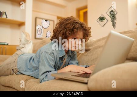 A curly-haired boy spending time on internet and looking involved Stock Photo