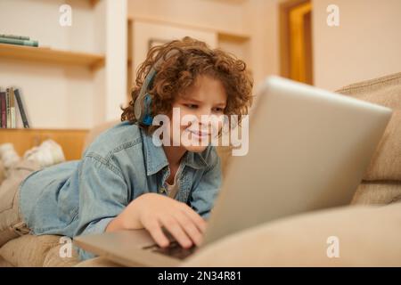 A curly-haired boy spending time on internet and looking involved Stock Photo