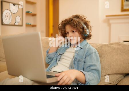 A curly-haired boy spending time on internet and looking involved Stock Photo