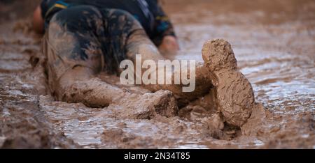 Mud race runners. Crawling, passing under a barbed wire obstacles during extreme obstacle race. Focus on the shoe Stock Photo