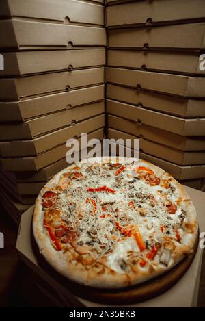 Many cardboard boxes of pizza. The boxes are on top of each other with one pizza between them. Stock Photo
