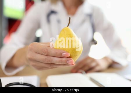 Close-up of pear in hand of nutritionist above medical office table. Stock Photo
