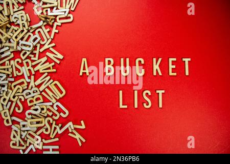 A BUCKET LIST in wooden English words language capital letters spilling from a pile of letters on a red background Stock Photo