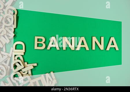 BANANA in wooden English language capital letters spilling from a pile of letters on a green background framed Stock Photo